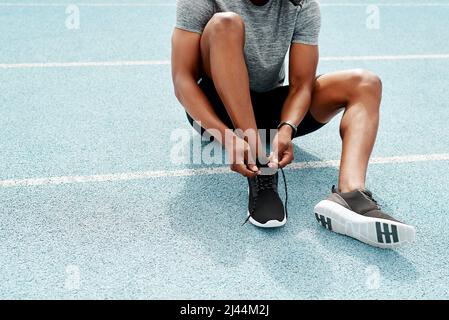 Sicherstellen, dass meine Schnürsenkel fest gebunden sind. Kurzer Schuss eines nicht erkennbaren Athleten, der sitzt und seine Schnürsenkel bindet, bevor er alleine laufen kann. Stockfoto