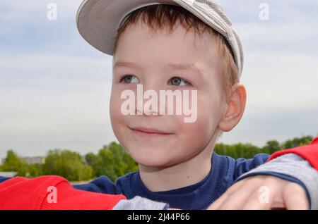 kaukasischer Junge in einer Baseballmütze lächelt und träumt blickt in den grünen Park in der Ferne Stockfoto