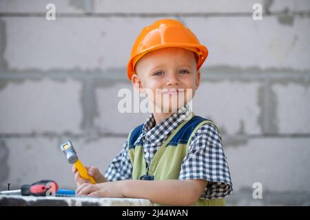 Niedliches kleines Kind im Bauhelm mit Reparaturwerkzeugen auf der Baustelle. Kind Junge in einem Bauhelm arbeiten hart. Glücklich lächelnde Kinder Stockfoto