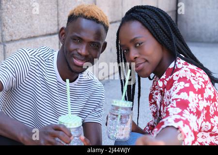 Junges afrikanisches Paar, das ein Selfie macht und Erfrischungen trinkt. Stockfoto