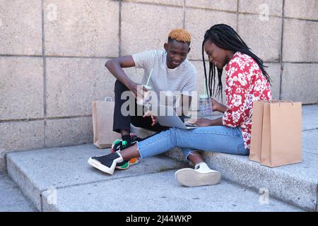 Junges schwarzes Paar lächelt, überprüft einen Laptop, trinkt Erfrischungen. Stockfoto
