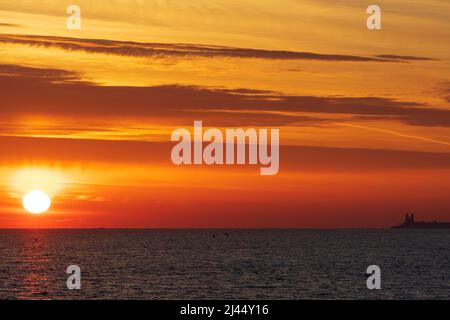 HERNE BAY: Die Sonne geht an einem kühlen Aprilmorgen über dem Meer auf, die Türme aus dem 12.. Jahrhundert in Reculver sind in der Ferne zu sehen. Stockfoto