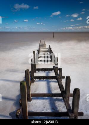 Lange Exposition von Wellen, die über Holzgroyne Rollen, Overstrand Beach, Norfolk, Großbritannien Stockfoto