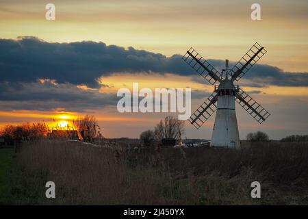 Wunderschöner oranger Sonnenuntergang über der Deichmühle Thurne Dyke in The Broads, Norfolk Stockfoto