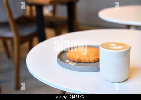 Der morgendliche Brunch im Café ist auf dem Tisch. Riesenkeks und Cappuccino mit schönem Milchschaum. Manchmal muss man in dieser schnelllebigen Welt eine Pause einlegen Stockfoto