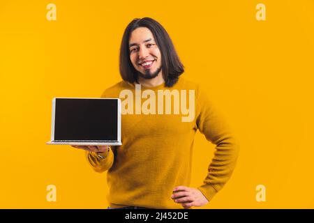 Der junge europäische Mann zeigt einen geöffneten Laptop mit einem schwarzen Bildschirm, lächelnd mit einer Hand auf seiner Taille Werbekonzept isoliert Studio Shot Medium Shot Copy Space . Hochwertige Fotos Stockfoto