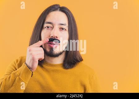 Mittlere Nahaufnahme junge langhaarige Mann berühren gefälschte schwarzen Schnurrbart gelben Hintergrund Kopie Raum isoliert Studio Schuss movember . Hochwertige Fotos Stockfoto