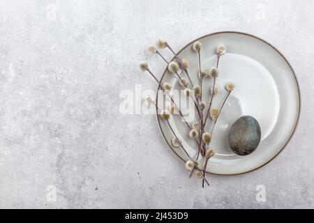 Osterbild mit bemalten Eiern auf einem Teller. Weidenzweig. Das Minimalkonzept von Ostern. Eine Osterkarte mit Platz für den Text. Stockfoto