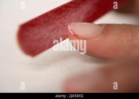 Der Prozess der Ablage von Nägeln. Rote franzosen abschneiden. Weibliche Maniküre aus nächster Nähe Stockfoto