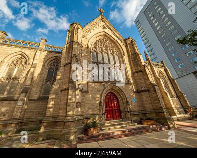 Westfassade der Mill Hill Chapel mit ihren hellroten Türen und einem modernen mehrstöckigen Gebäude dahinter Stockfoto