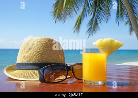 Sonnenhut mit Sonnenbrille und Fruchtsaft unter Palmen am Strand in Thailand Stockfoto