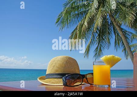 Sonnenhut mit Sonnenbrille und Fruchtsaft unter Palmen am Strand in Thailand Stockfoto