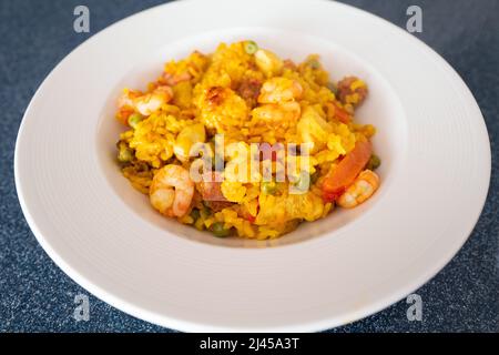 Garnelen und Chorizo-Wurst in einem hausgemachten Reis-Paella-Gericht. Es gibt auch Huhn mit Zwiebeln, Erbsen und Paprika in der Mahlzeit. Es wird in einer runden Wh serviert Stockfoto
