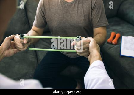 Asiatische männliche Physiotherapeut Abstieg Arbeit und helfen, die Hände von Patienten mit Patienten tun Stretching-Übung mit einem flexiblen exer zu schützen Stockfoto