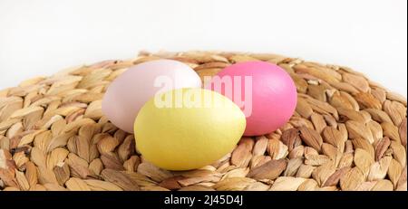 Bunte Ostereier in einem Korb auf weißem Holztisch. Burlap-Hintergrund. Frohe Ostern. Rustikales, umweltfreundliches Konzept. Gefärbte Eier auf einer Strohnapkin. Stockfoto