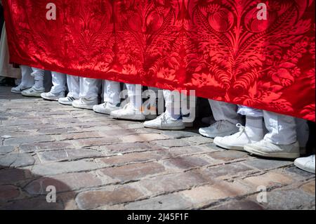 Caus, Spanien. 11. April 2022. Die Füße der Männer, die einen schweren Thron tragen, während die Menschen an den traditionellen Paraden der Semana Santa oder der Karwoche in Cdiz Spanien teilnehmen. Jeden Tag in dieser Woche nehmen die Bruderschaften an spektakulären Prozessionen und Marschkapellen in der Stadt Teil, die riesige Throne führen, die Jesus am Kreuz und die Jungfrau Maria darstellen. Viele tragen traditionelle Roben und hochspitz zulaufende Hüte. Kredit: Julian Eales/Alamy Live Nachrichten Stockfoto