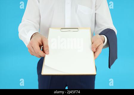 Kellner mit Klemmbrett. Männlicher Kellner in Schürze, der ein leeres Klemmbrett auf blauem Hintergrund hält. Kellner mit Klemmbrett Stockfoto