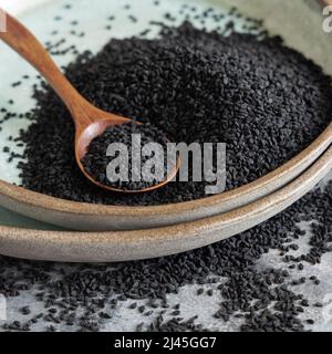 Teller mit indischen Gewürzen Schwarzer Kreuzkümmel (Nigella sativa oder Kalonji) Samen auf grauem Tisch mit einem Holzlöffel, Nahaufnahme. Traditionelle asiatische Medizin, gesund A Stockfoto