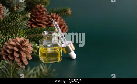 Glasflasche mit einem Tropf mit ätherischem Nadelöl in der Nähe von Tannenzweigen und Tannenzapfen auf Holzstück auf grünem Nahaufnahme. Aromatherapie, Spa und Herba Stockfoto