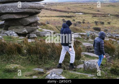 Menschen, die am Cheesewring vorbei an einem Granitfelsen-Stapel vorbeilaufen, der durch Gletscheraktionen auf Stowes Hill auf Bodmin Moor in Cornwall gebildet wurde. Stockfoto