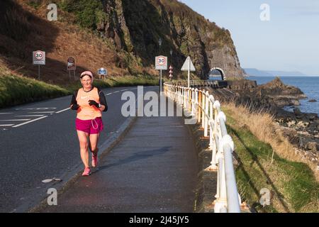 Jogger kurz vor der Drains Bay in Co. Antrim, Nordirland, an der Küstenstraße unweit von Larne, mit dem Black Arch im Hintergrund. Stockfoto