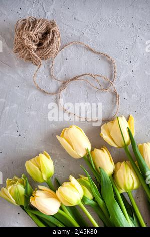 Ein Strauß gelber Tulpen mit Garn auf einem grauen Tisch anrichten. Stockfoto