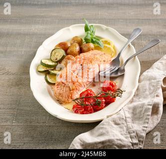 Teller mit gebratenem Lachsfilet und Gemüse auf einem hölzernen Küchentisch Stockfoto