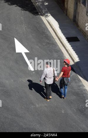 Touristikpaar Hände halten oder Hand in Hand gehen und Weißer Pfeil auf der Straße nach vorne zeigen Aigues-Mortes Gard Frankreich Stockfoto