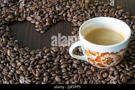 Eine Tasse Kaffee, umgeben von Kaffeebohnen, in denen das Herz zubereitet wird Stockfoto