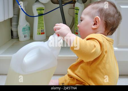 Kleinkind Baby Junge spielt mit Wasch-und Reinigungsmittel in einem offenen Küchenschrank. Probleme mit der Kindersicherheit im heimischen Zimmer, kleines Kind Stockfoto