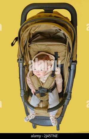 Ein glückliches Kind sitzt in einem Kinderwagen auf einem gelben Hintergrund. Lächelndes Kleinkind Baby in einem Transformator Kinderwagen für den Transport von Kindern Stockfoto