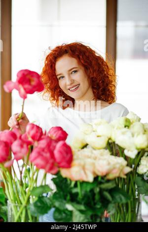 Floristin bei der Arbeit: Hübsche junge Rothaarige Frau macht Mode modernen Strauß von verschiedenen Blumen Stockfoto