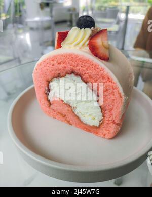Frisches Stück Strawberry Swiss Roll Cake mit frischem Rahm Belag mit Erdbeer- und Heidelbeerpaste auf weißer Schale. Stockfoto