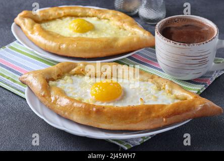 Khachapuri in Adjarian, Offene Torten mit Suluguni-Käse und Eigelb in Form eines Bootes auf Tellern auf grauem Hintergrund, traditionelle georgische Küche Stockfoto