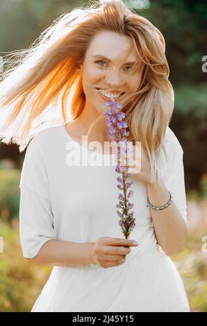 Заголовок Junge Blondine mit kurzen Haaren in einem sommerlichen weißen Kleid. Frau posiert in einem Lupinenfeld Stockfoto