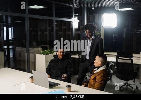 Eine multiethnische Gruppe afrikanischer und asiatischer Kollegen arbeitet an einem Laptop für ein Geschäftsprojekt. Zwei schwarze, gutaussehende Manager arbeiten mit einem asiatischen Mann und Stockfoto
