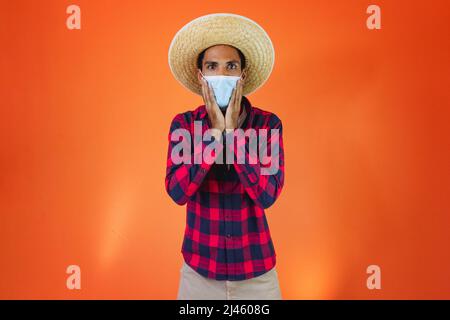 Schwarzer Mann mit Junina Party Outfit isoliert auf orangefarbenem Hintergrund. Junger Mann in traditioneller Kleidung für Festa Junina - brasilianisches Juni-Festival. Stockfoto