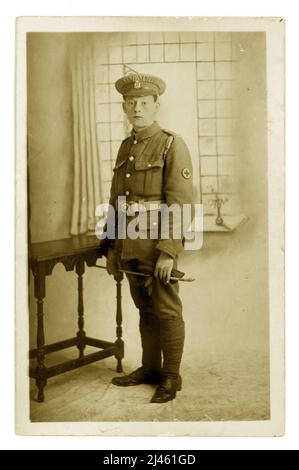 Original Postkarte Studio Porträt von WW1 Ära ersten Weltkrieg Red Cross Freiwilligen oder VAD, wie sie bekannt waren. Er hieß Charlie und er sieht sehr müde aus, vielleicht zu viel an der Front gesehen zu haben. Er hält eine Reiternte, was bedeuten könnte, dass er mit Pferden gearbeitet hat, um die Verwundeten aus den Gräben zurückzuholen. Aus Richtung Ye Olde Guildhall Studio, 29 St. Thomas St. Winchester 1914-1918. Stockfoto