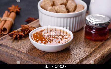 Köstliche Aprikosenmarmelade, Milch und Zucker auf einem Holzschneidebrett vor dunklem Betonboden Stockfoto