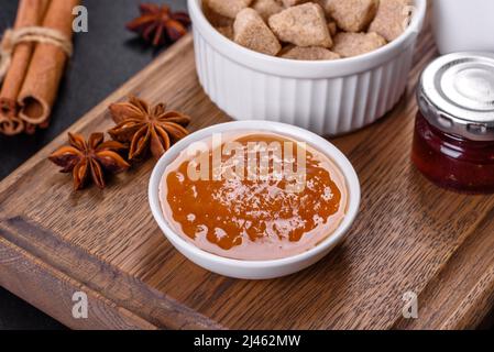Köstliche Aprikosenmarmelade, Milch und Zucker auf einem Holzschneidebrett vor dunklem Betonboden Stockfoto