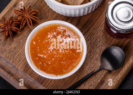 Köstliche Aprikosenmarmelade, Milch und Zucker auf einem Holzschneidebrett vor dunklem Betonboden Stockfoto