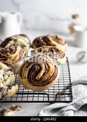 Zimtbrötchen Rollen oder Brioche auf Backgestell mit Leinenserviette auf hellem Hintergrund wirbeln. Zusammensetzung des morgendlichen Gebäcks Stockfoto