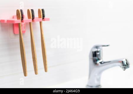 Drei natürliche Bambus-Zahnbürsten mit schwarzen Borsten in einem Halter vor einem gefliesten Hintergrund an der Badezimmerwand über dem Waschbecken. Selektiver Fokus. Stockfoto