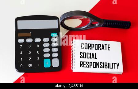 CSR Corporate Social Responsibility Konzept auf einem Notizblock mit Rechner und Lupe auf rot-weißem Hintergrund Stockfoto