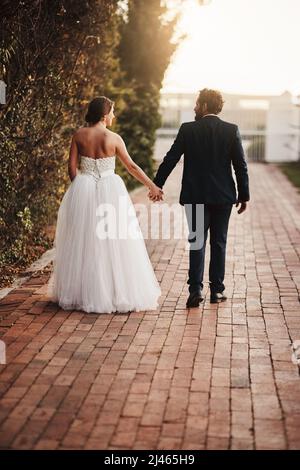 Gehen Sie vielleicht immer gemeinsam durch das Leben. Rückansicht eines Paares, das am Hochzeitstag zusammenläuft. Stockfoto