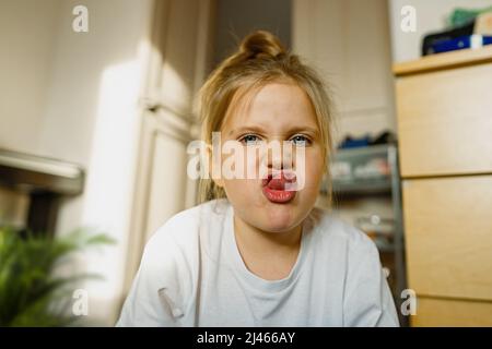 Lustige, kleine Mädchen mit blauen Augen zu Hause auf dem Boden spielt und Grimassen, macht Gesichter in die Kamera. Kopfschuss, Nahaufnahme Stockfoto