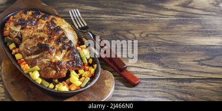 Hausgemachtes gebratenes Schweinefleisch in Bratpfanne mit geschnittenem Gemüse auf Eichenholz-Hintergrund mit Kopierfläche Stockfoto