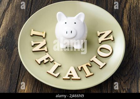 Inflation in Buchstaben und Sparschwein auf dem Teller geschrieben. Konzept zur Inflation von Lebensmitteln Stockfoto