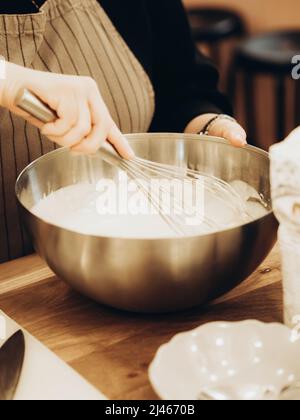Unbestimmte Frau mischte Teig mit Schneebesen in einer großen Metallschüssel. Home Bäcker Whisking Teig Zubereitung von köstlichen Mahlzeit Stockfoto