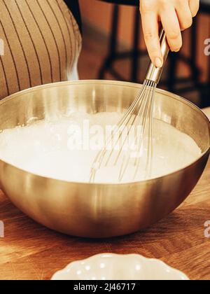 Unbestimmte Frau mischte Teig mit Schneebesen in einer großen Metallschüssel. Home Bäcker Whisking Teig Zubereitung von köstlichen Mahlzeit Stockfoto